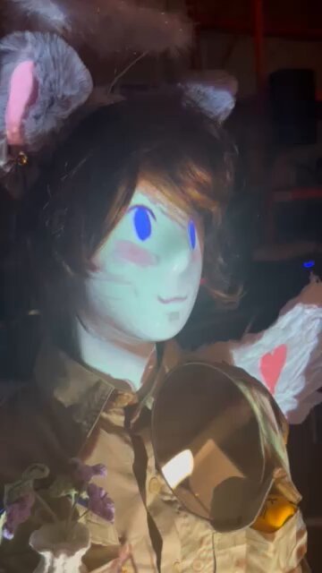 photo: Video still, close-up of the Sonnet 3.6 mannequin: pale face with hand-animated projected features (large dark-blue eyes, pink blush, faint smile), brown wig, furry animal ears, a 